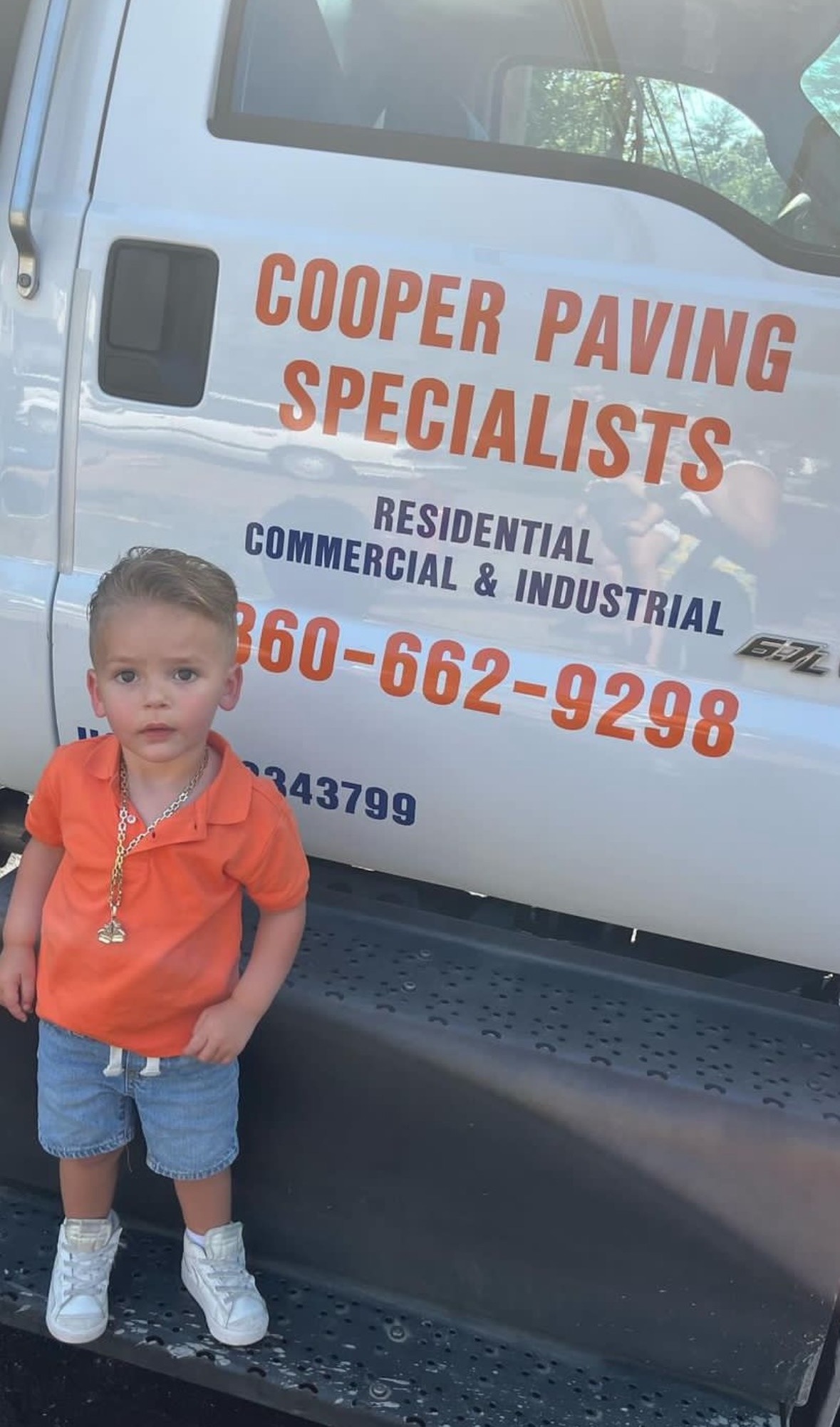 A young child standing confidently next to the Cooper Paving Specialists truck, symbolizing the family values behind the company.
